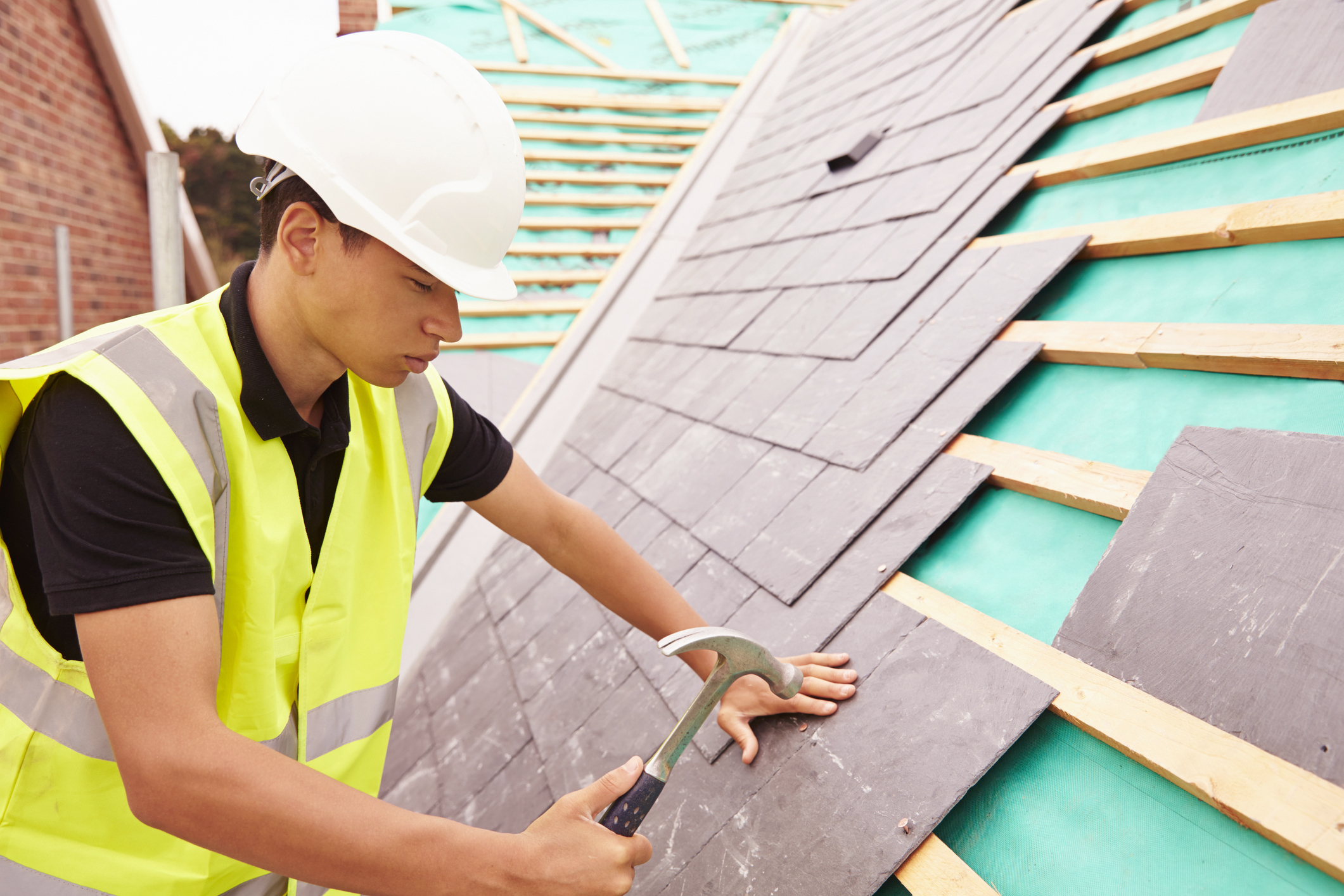 Construction worker in hard hat nailing slate onto roof