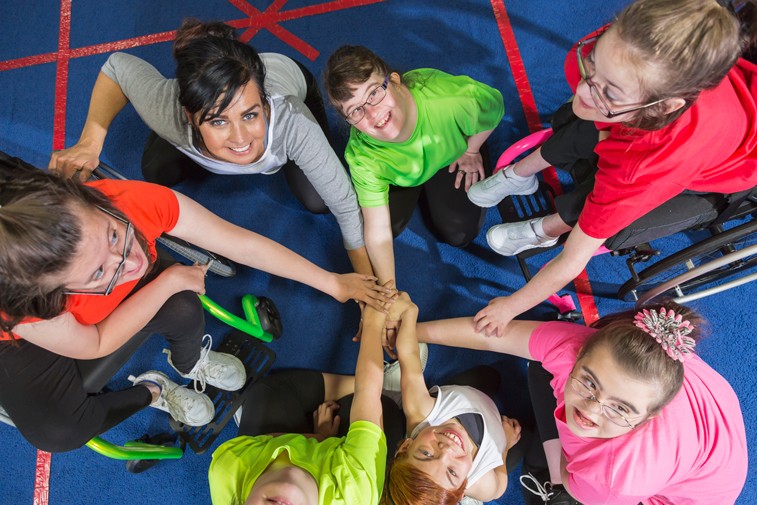 Group of children with their hands in the middle looking up to where the camera is