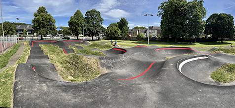 Tarmacked pump track for biking, built on grassy field with trees in distance
