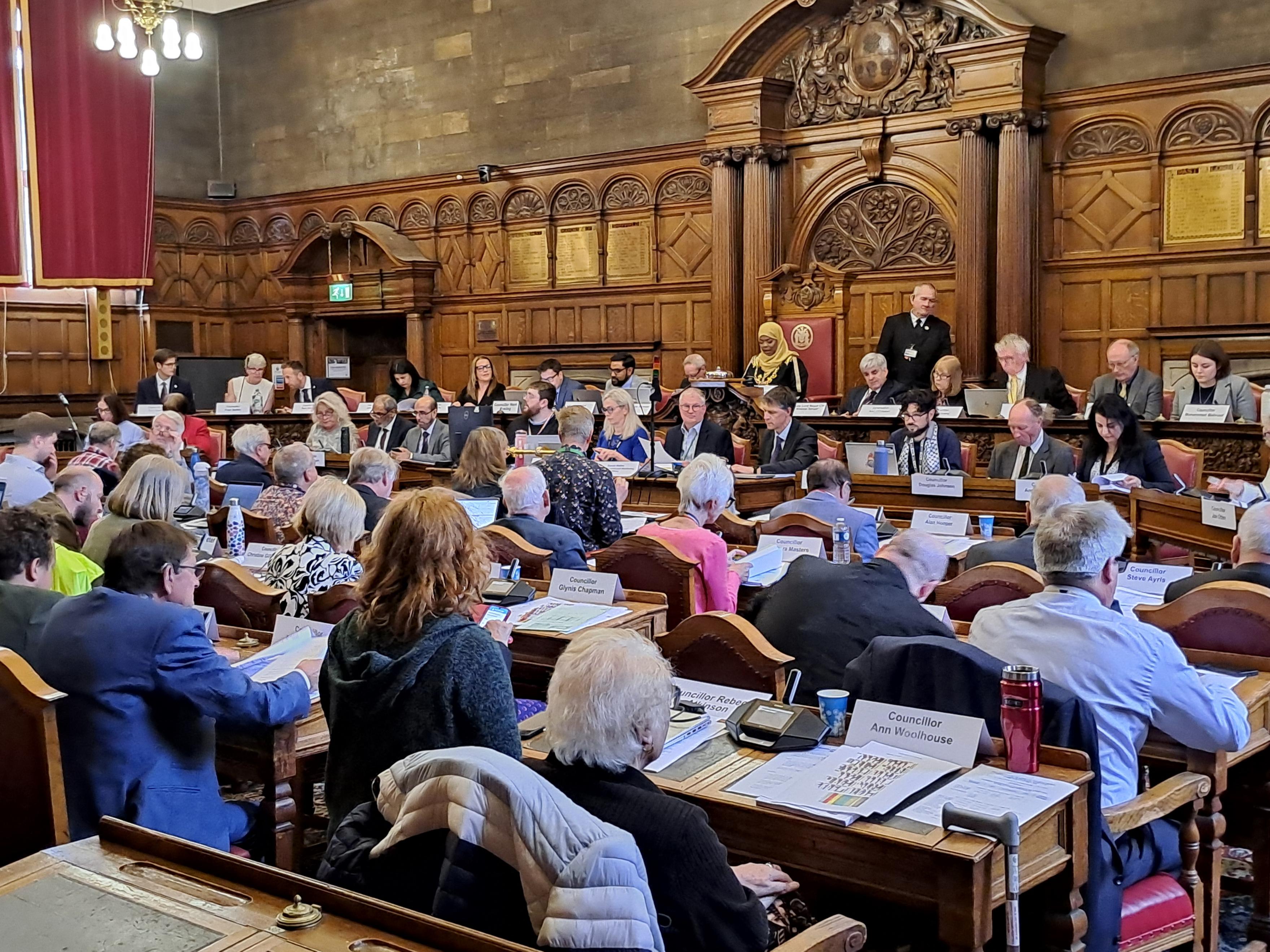 Councillors sit at their desks in a packed Council Chamber at Sheffield Town Hall during the 2025 Sheffield City Council AGM. The Council leadership face the room sitting at the top benches.