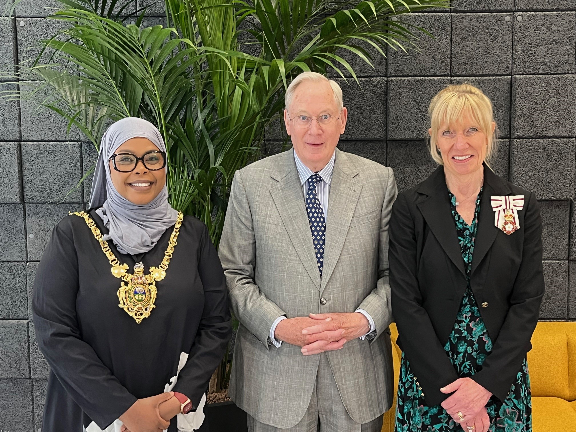 Three people, including the Lord Mayor of Sheffield, who is wearing the Lord Mayor's chains, stand in front of a dark background, they are all looking towards the camera and smiling