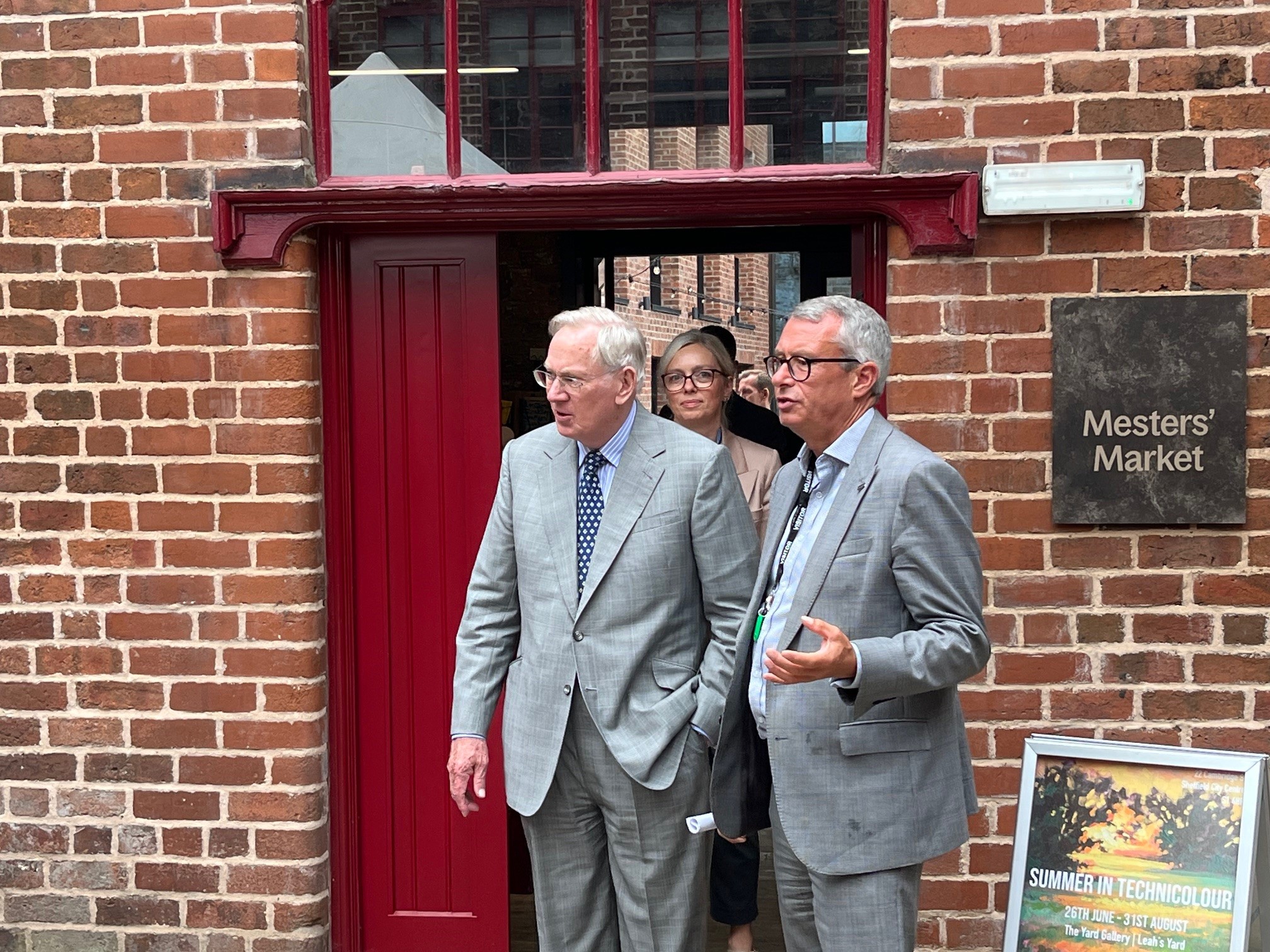A group of people emerge from a doorway at Leah's Yard, a sign on the right hand side wall reads 'Mesters Market'
