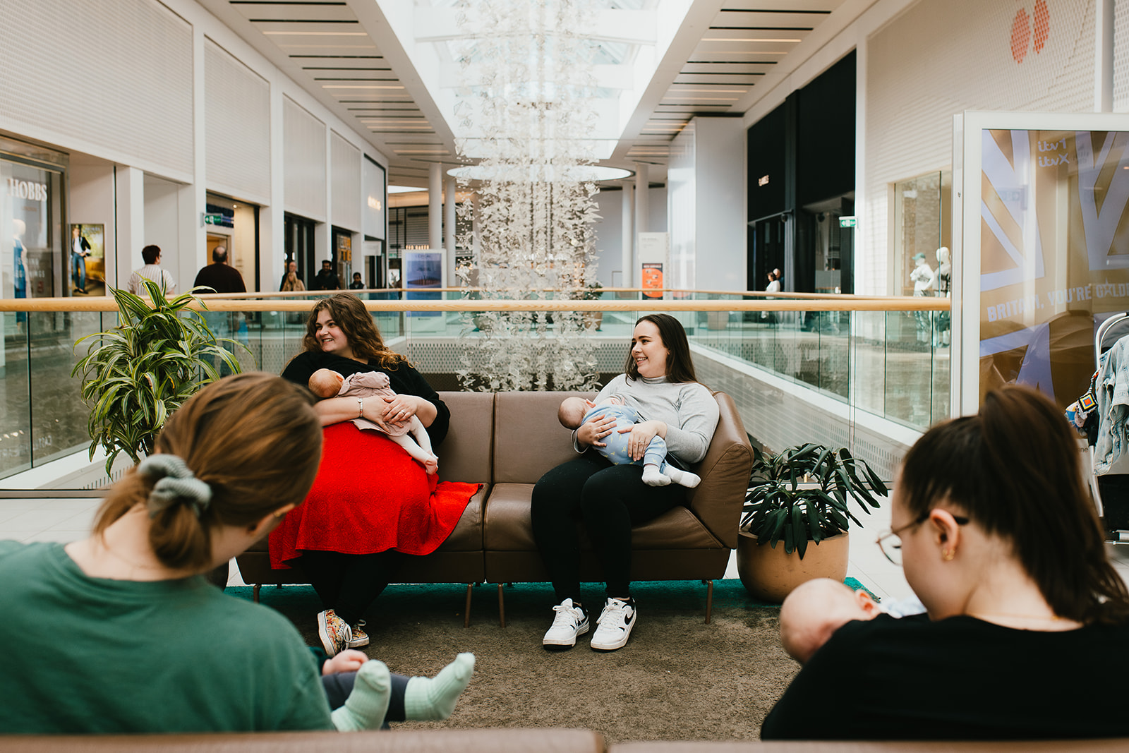 Parents breastfeeding and socialising at Meadowhall Shopping Centre sat on sofas in a communal area of the shopping centre