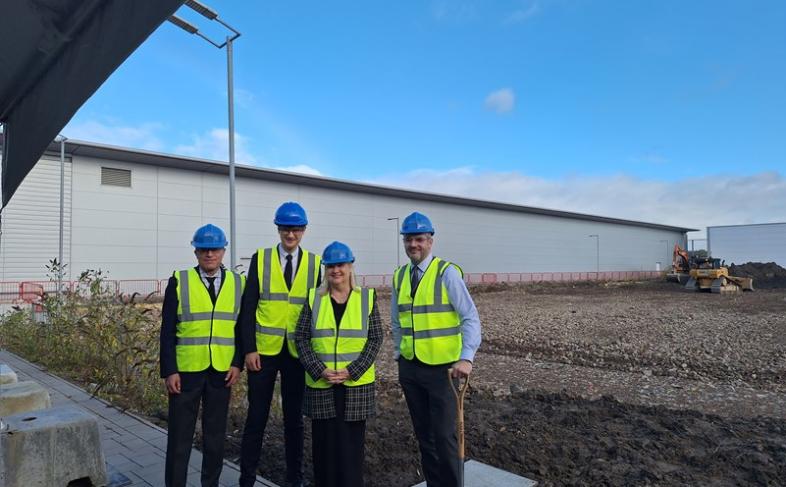 four people wearing yellow hi viz jackets and blue hard hats. They are stood outside with a blue sky overhead