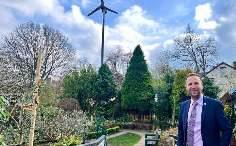Cllr Ben Miskell in a park, standing in front of a wind turbine