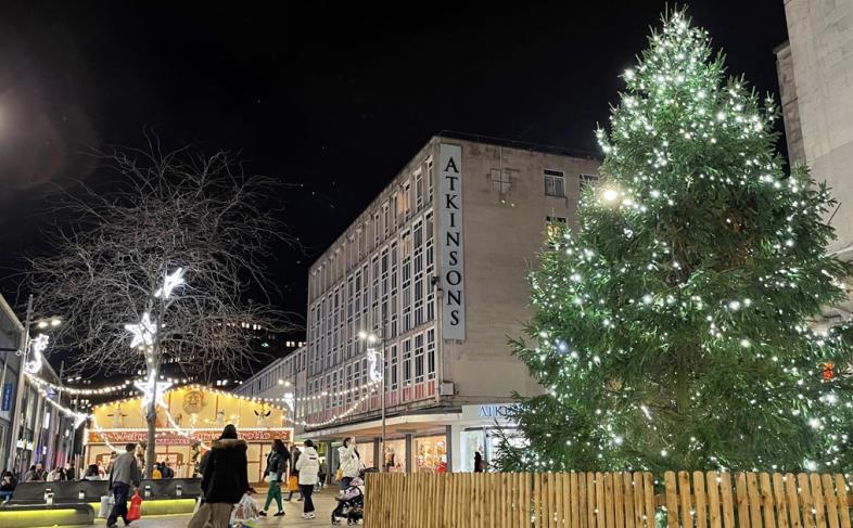 Image of The Moor at Christmas. There is a Christmas tree and Atkinson's store on the right. There are Christmas lights and people walking around