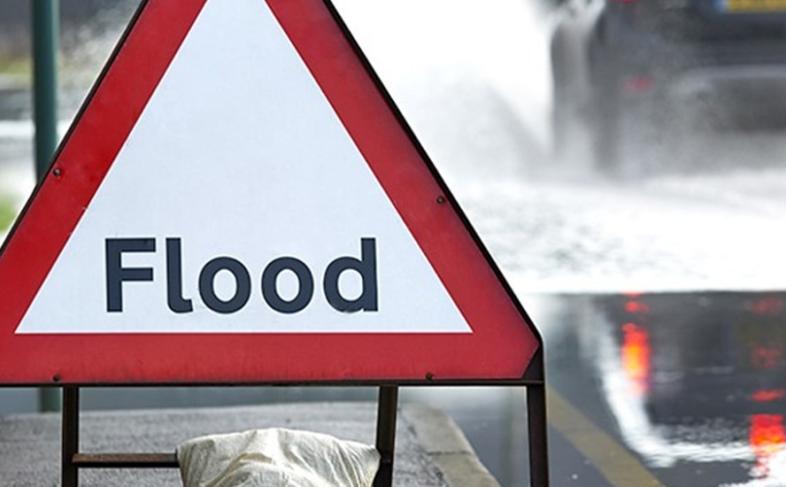 An image of a flood warning sign with cars going past on the road spraying water