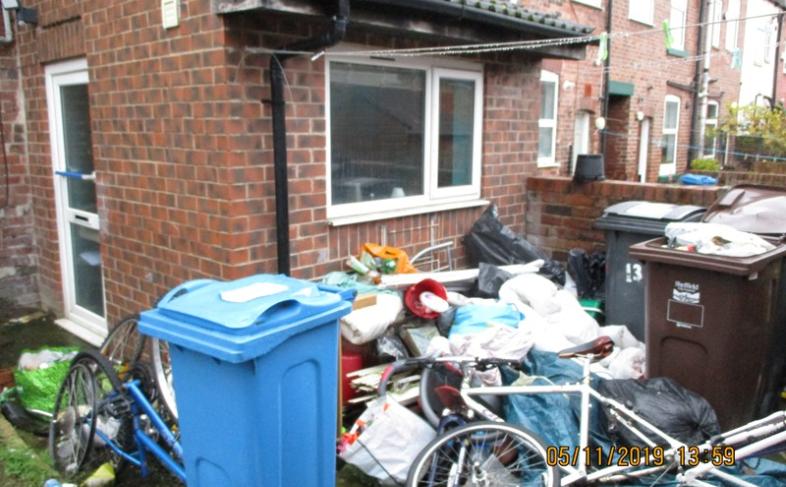 A house with a front garden full of hazardous items including and old bike and bags of rubbish