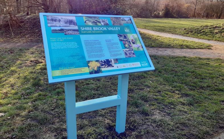 Blue sign for Shire Brooke Valley Nature Reserve with grass and trees in the background