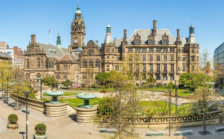 A picture of Sheffield Town Hall with the building in the back ground and the Peace Gardens in the foreground surrounded with trees.