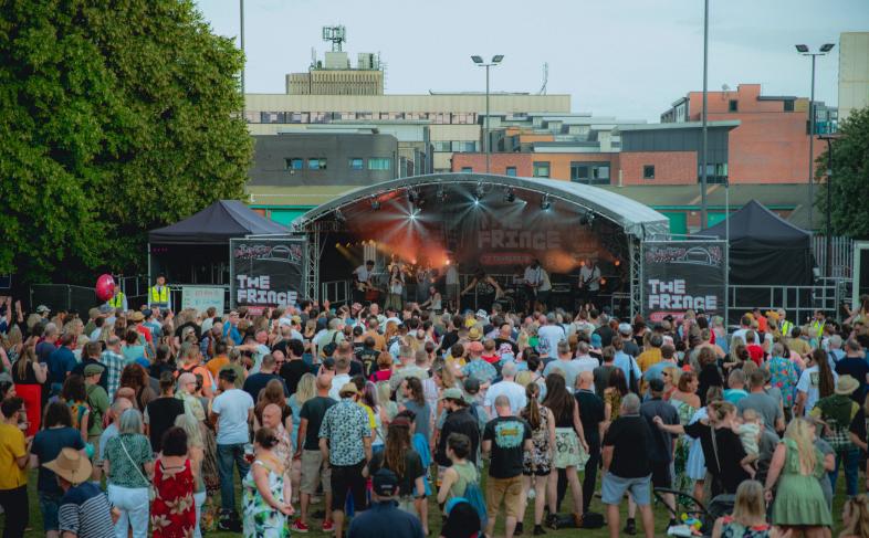 Devonshire Green main stage with crowds in front and brown buildings in the distance