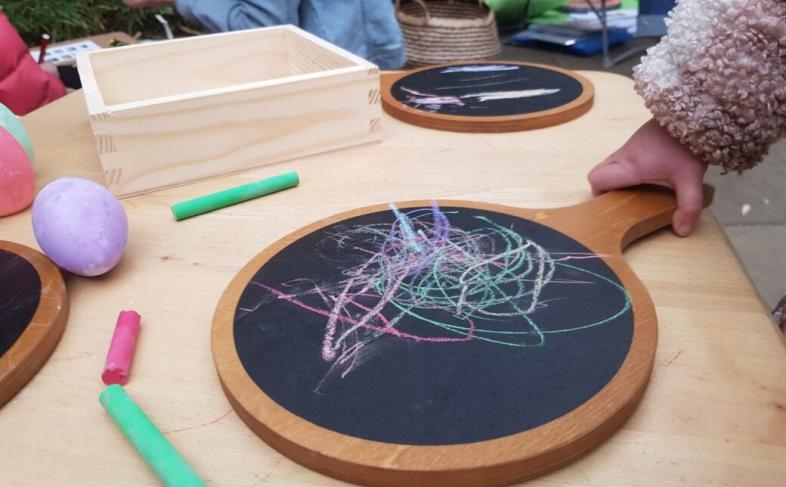 A child holds a chalk board on which they have doodled, with other children and chalk boards in the background