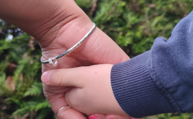 An adult and a child hold hands in a garden with a hedge in the background