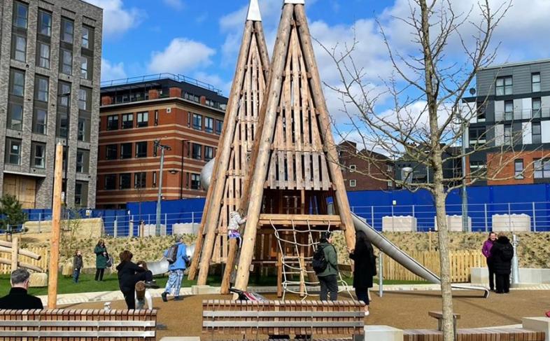 A picture of Pounds Park children's play area under a blue sky with white clouds and surrounded by taller buildings
