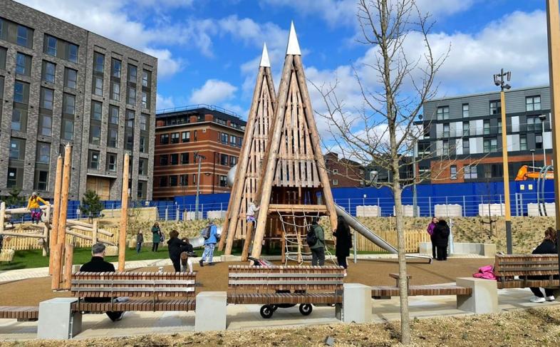 A picture of Pounds Park children's playground on a summers day with blue sky and white clouds in the sky, the park is surrounded by tall buildings on all sides