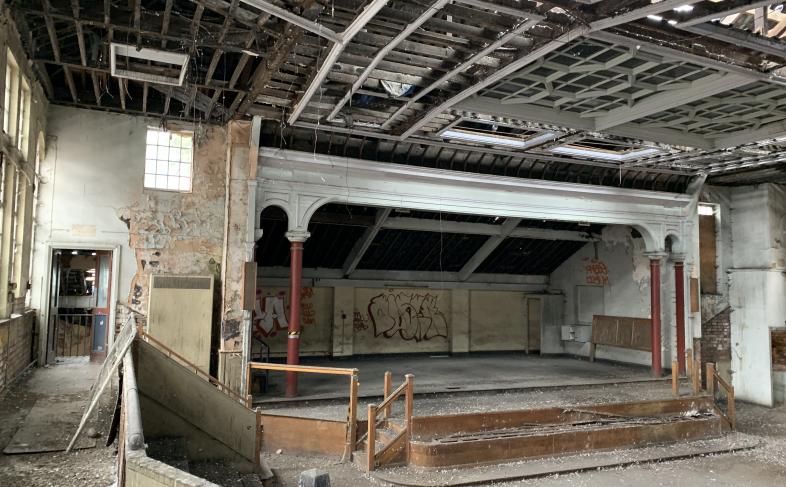 A view inside the former Salvation Army Citadel building looking towards the stage area with a bank of seats on the left hand side.