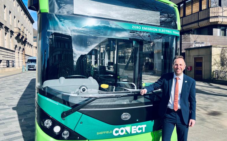 Cllr Ben Miskell stands in front of a green Sheffield Connect electric bus on a beautiful sunny day.
