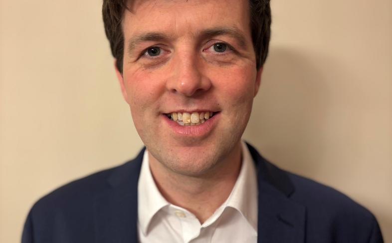 James Clark smiles for the camera stood in front of a plain wall