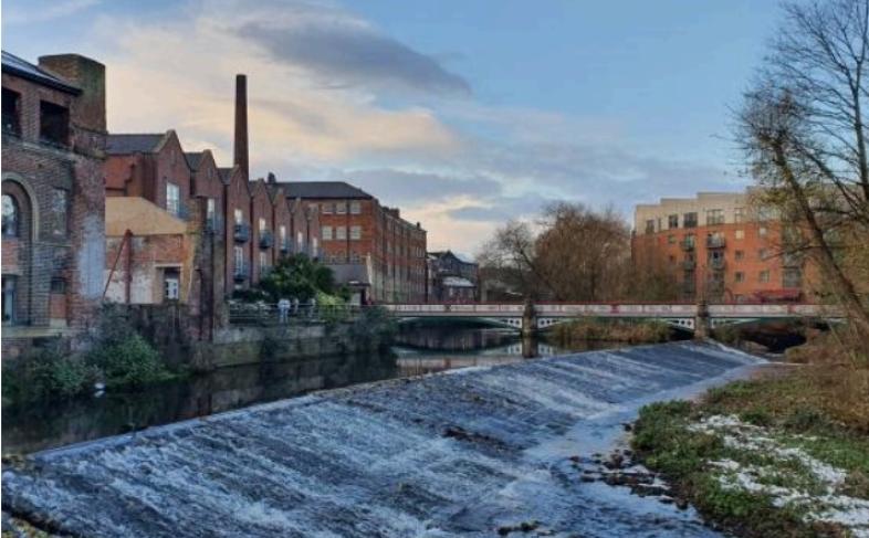 Dusk falls over the weir at Kelham Island as shadows fall on the water caused by the large industrial and residential buildings next to the water