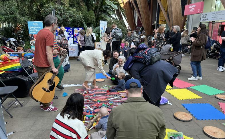 Parents coming together to discuss breastfeeding and other parenting issues at an event in The Winter Garden in Sheffield. Many are sat on the floor chatting while others have a chat standing in between them