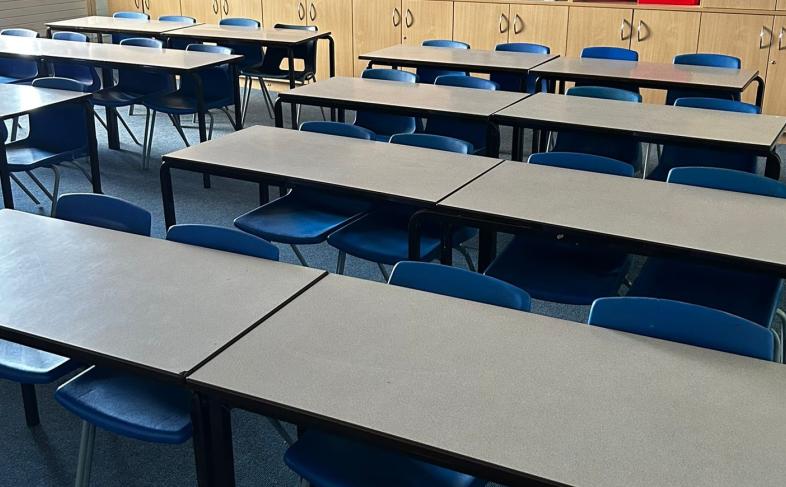 Blue plastic chairs and cream-coloured tables lined up in a classroom, ready for a lesson to begin