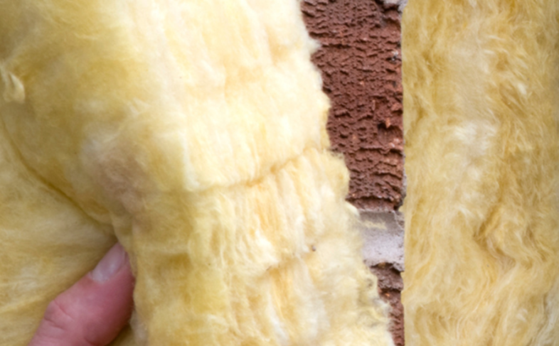 A close-up image of yellow wall insulation being put in place by hand as a property is constructed