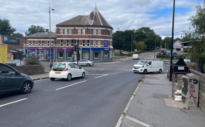 Cars queue at a cross roads with a yellow hatched box marked on the road in the middle of the cross roads