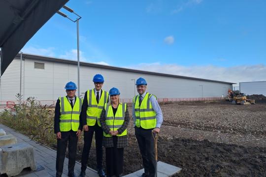four people wearing yellow hi viz jackets and blue hard hats. They are stood outside with a blue sky overhead