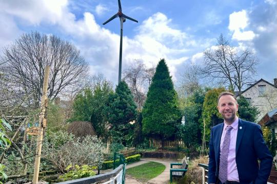 Cllr Ben Miskell in a park, standing in front of a wind turbine