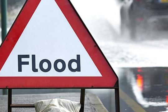 An image of a flood warning sign with cars going past on the road spraying water