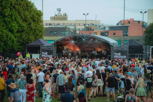 Devonshire Green main stage with crowds in front and brown buildings in the distance