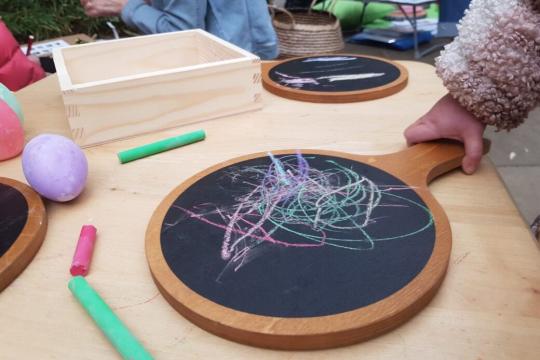 A child holds a chalk board on which they have doodled, with other children and chalk boards in the background