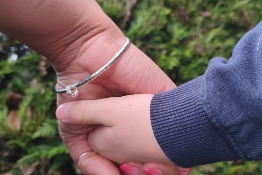 An adult and a child hold hands in a garden with a hedge in the background