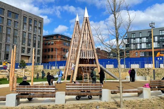 A picture of Pounds Park children's playground on a summers day with blue sky and white clouds in the sky, the park is surrounded by tall buildings on all sides
