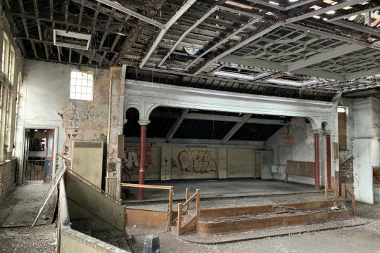 A view inside the former Salvation Army Citadel building looking towards the stage area with a bank of seats on the left hand side.