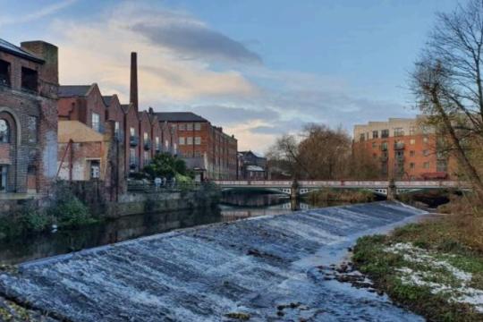 Dusk falls over the weir at Kelham Island as shadows fall on the water caused by the large industrial and residential buildings next to the water
