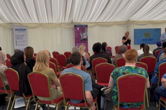 Seated attendees in a marquee area watch a presentation 