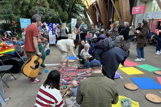 Parents coming together to discuss breastfeeding and other parenting issues at an event in The Winter Garden in Sheffield. Many are sat on the floor chatting while others have a chat standing in between them