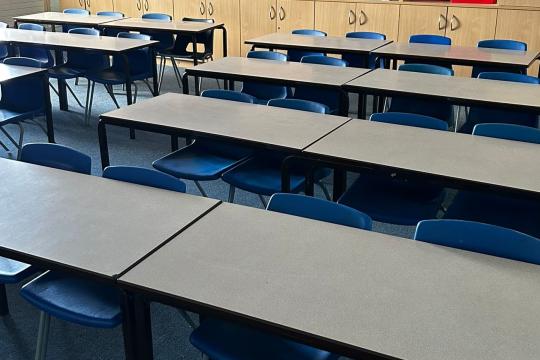 Blue plastic chairs and cream-coloured tables lined up in a classroom, ready for a lesson to begin