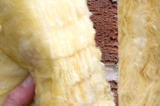 A close-up image of yellow wall insulation being put in place by hand as a property is constructed