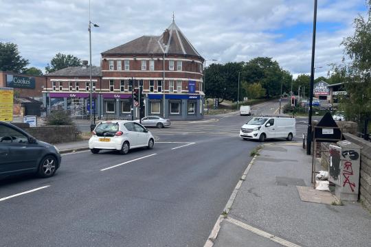 Cars queue at a cross roads with a yellow hatched box marked on the road in the middle of the cross roads